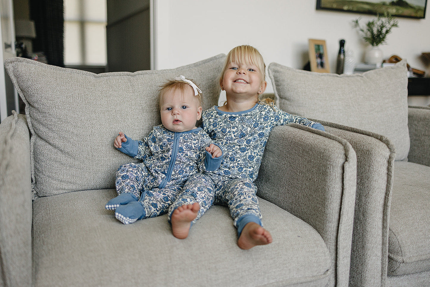 Two children in matching blue and white pajamas sitting on a couch.