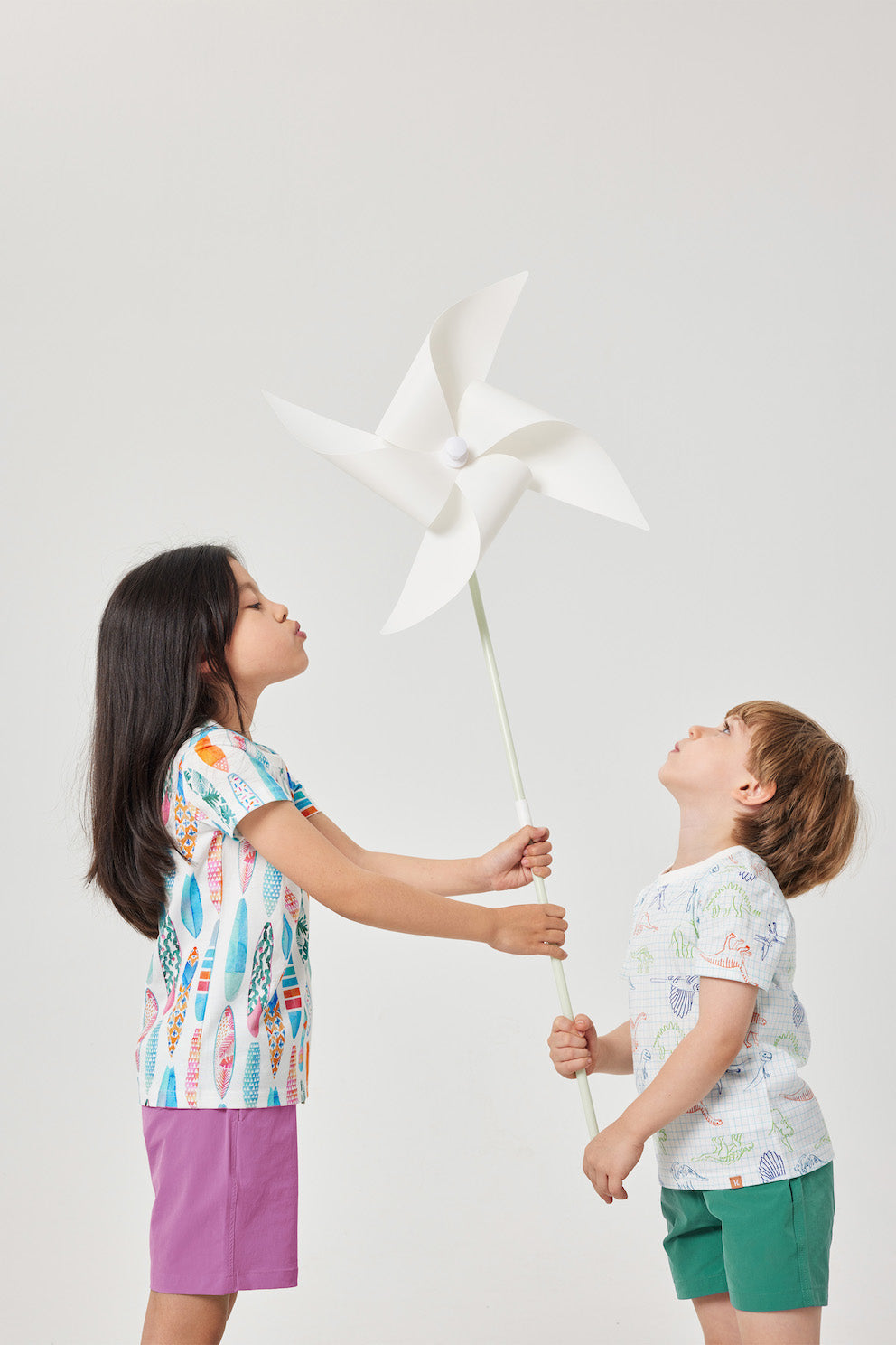 Two children playing with a white pinwheel against a plain background