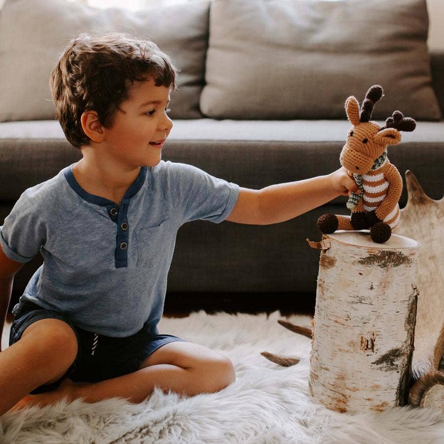 Child playing with a stuffed moose toy on a log in a cozy living room.