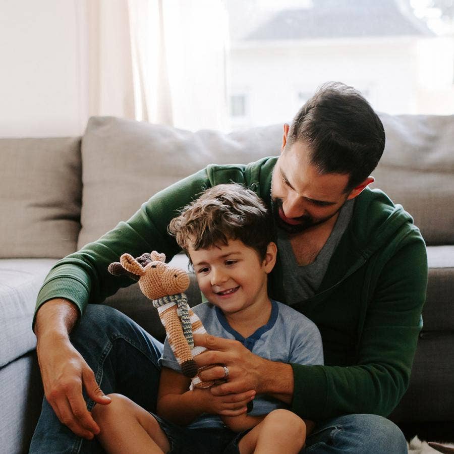 Man and child sitting in front of a couch with a moose toy, smiling