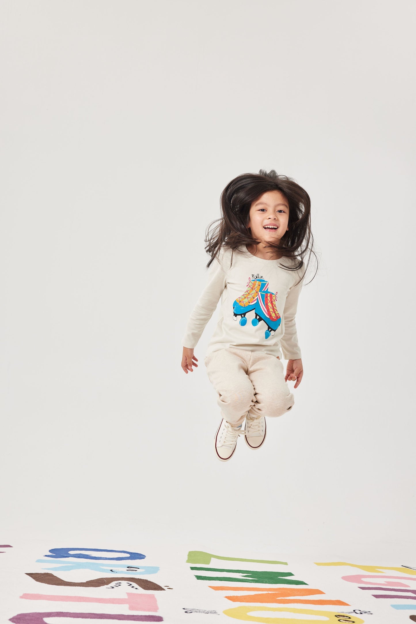 Child jumping in the air wearing a long-sleeve shirt with a colorful design on a white background