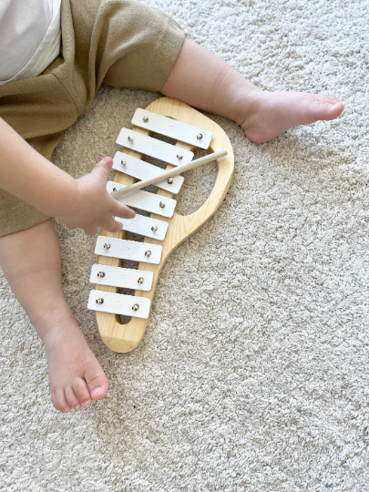 Child playing with a wooden xylophone on a carpeted floor