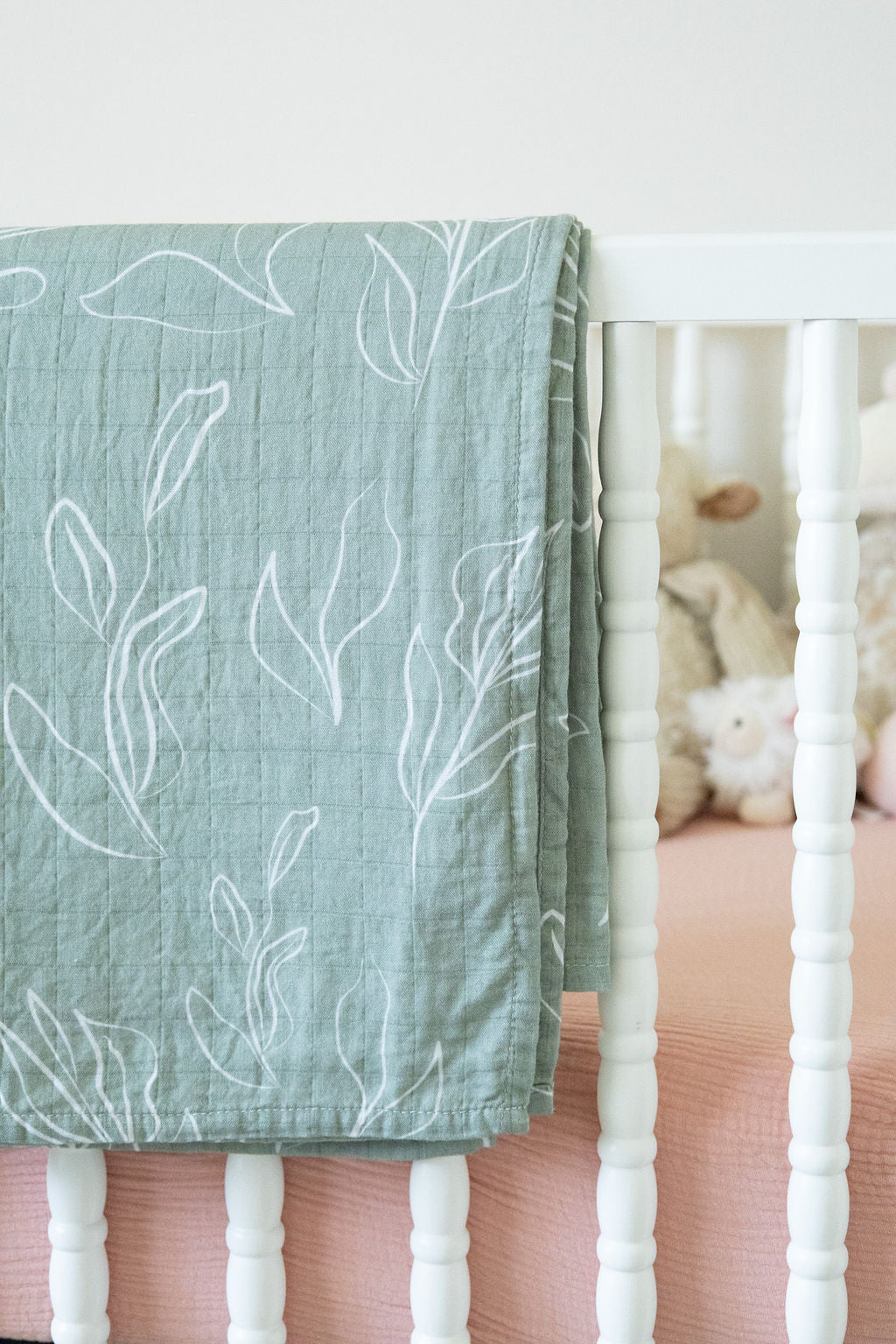 Green leaf-patterned blanket draped over a crib with white bedding.