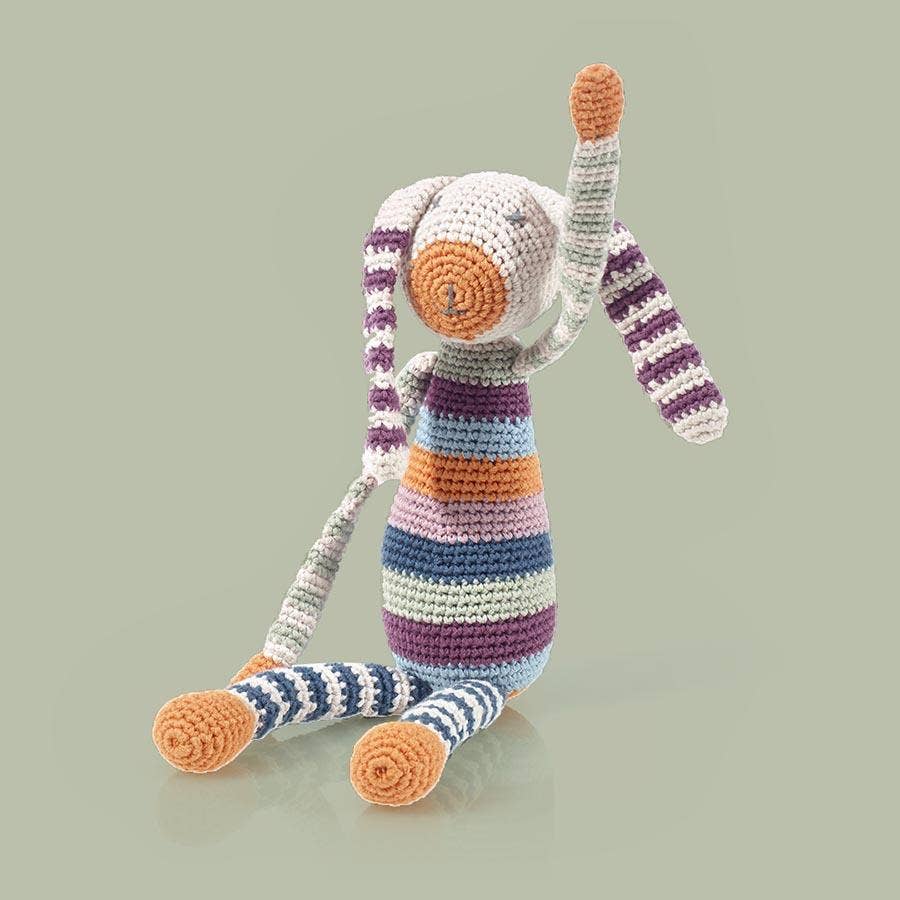 Striped crochet bunny toy with orange accents on a light gray background