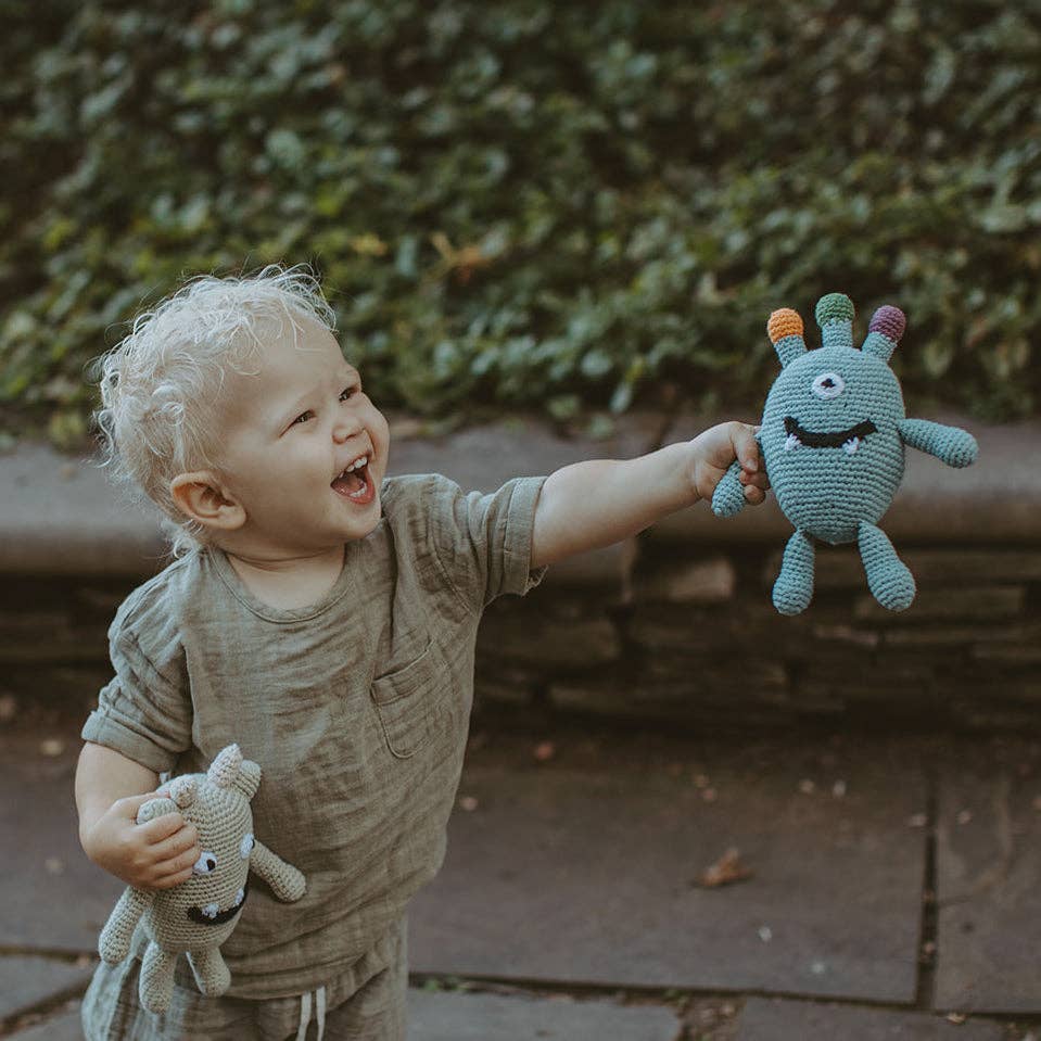 Child laughing and holding a knitted monster toy outdoors.