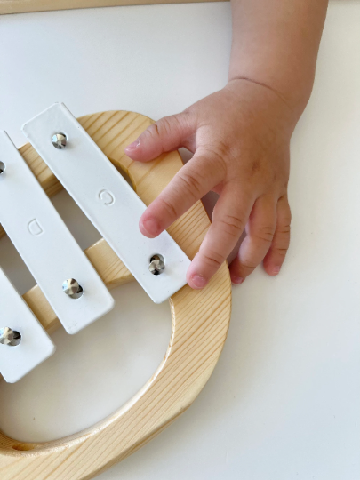 Child's hand playing a wooden xylophone on a white surface