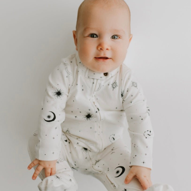 Baby wearing a white onesie with black celestial patterns on a plain background