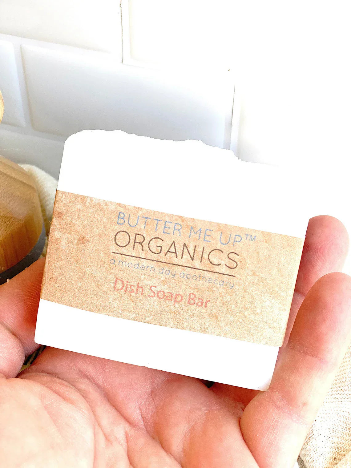 Butter Me Up Organics dish soap bar held in a hand with a blurred background