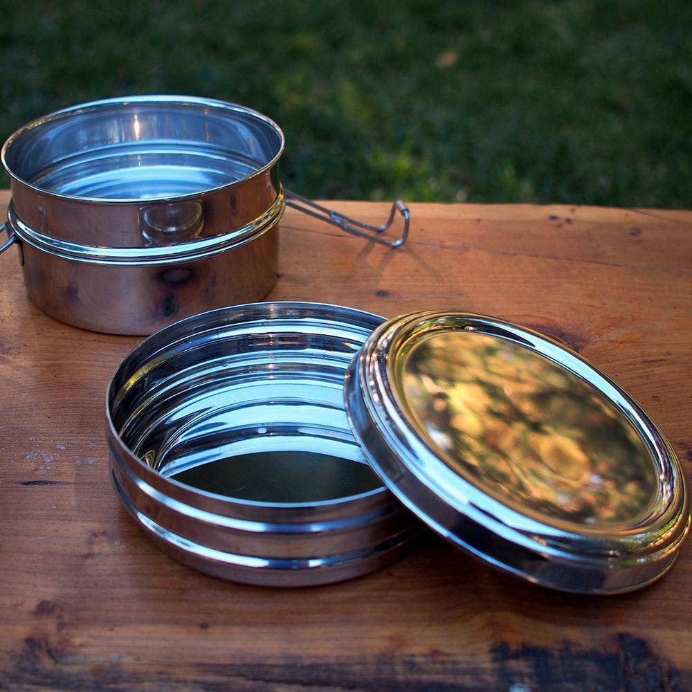 Metal 3-tier food containers with lids on a wooden table outdoors