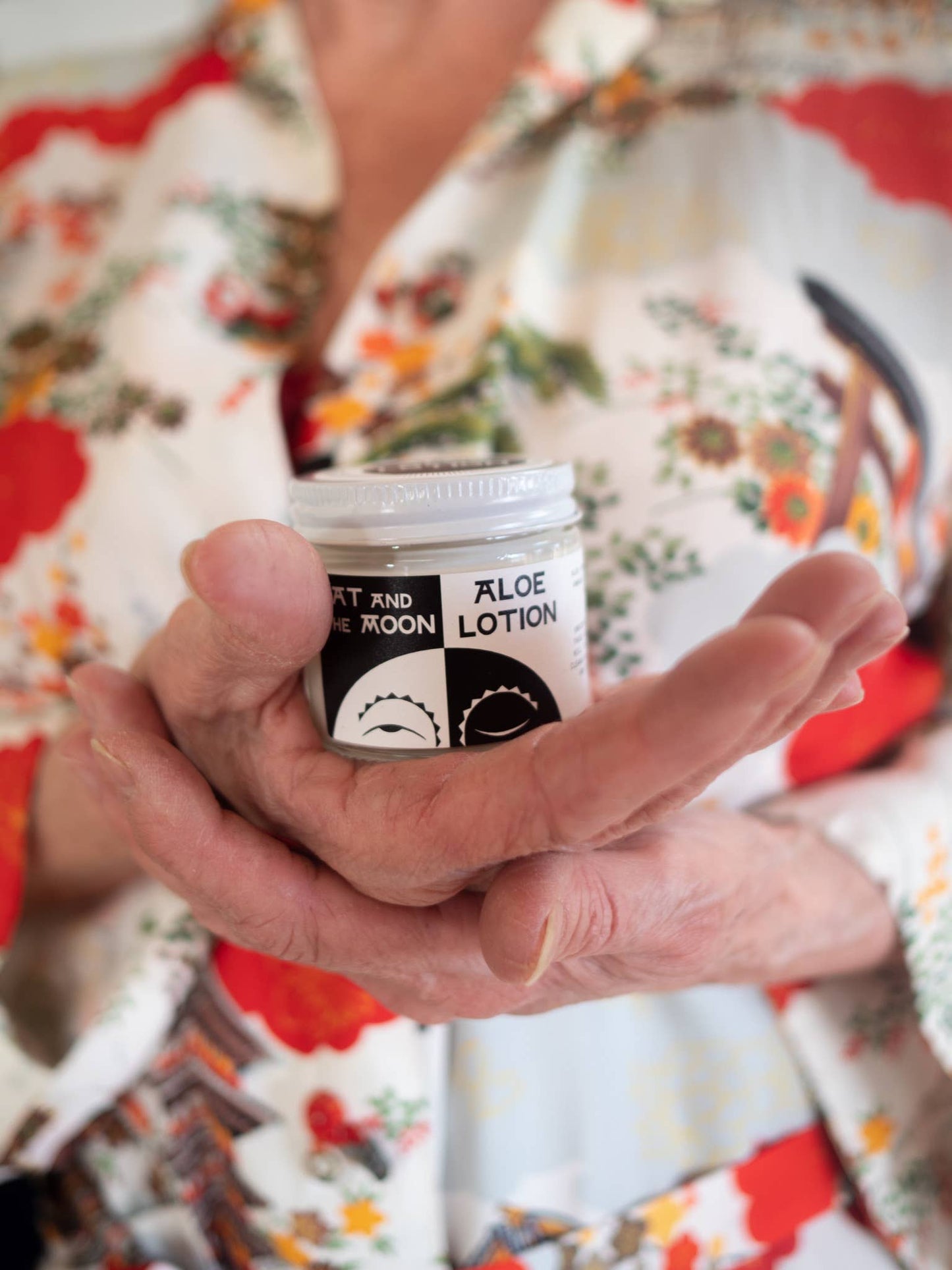 a person wearing a flower shirt holding a tub of aloe lotion in their hands
