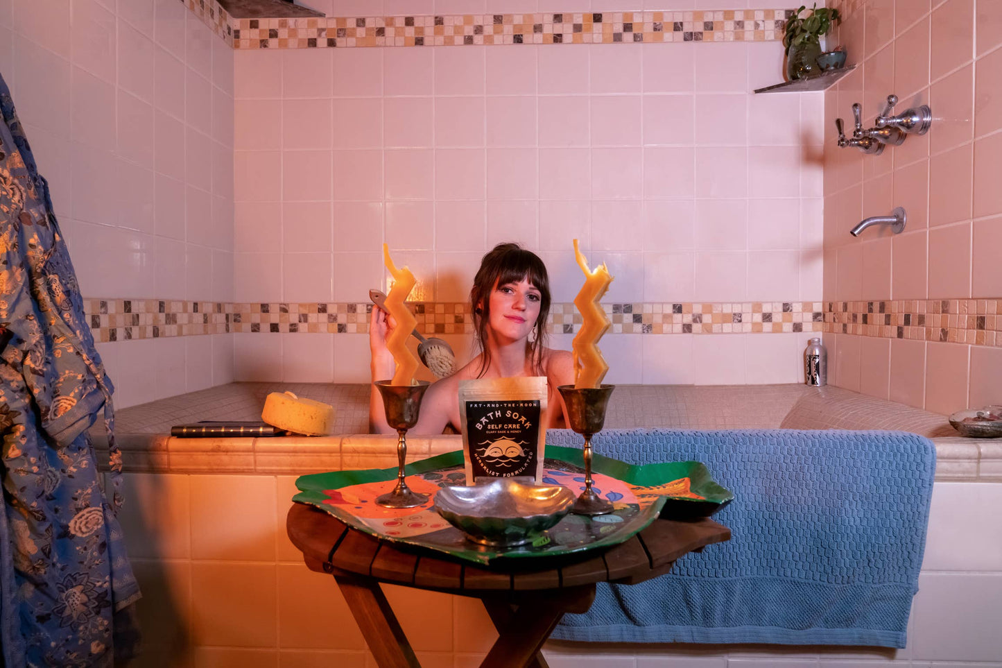 a person sitting in a bathtub with bath soak and candles on a table