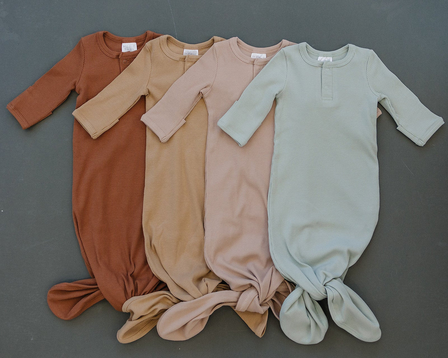 Four baby onesies in different colors arranged on a gray background