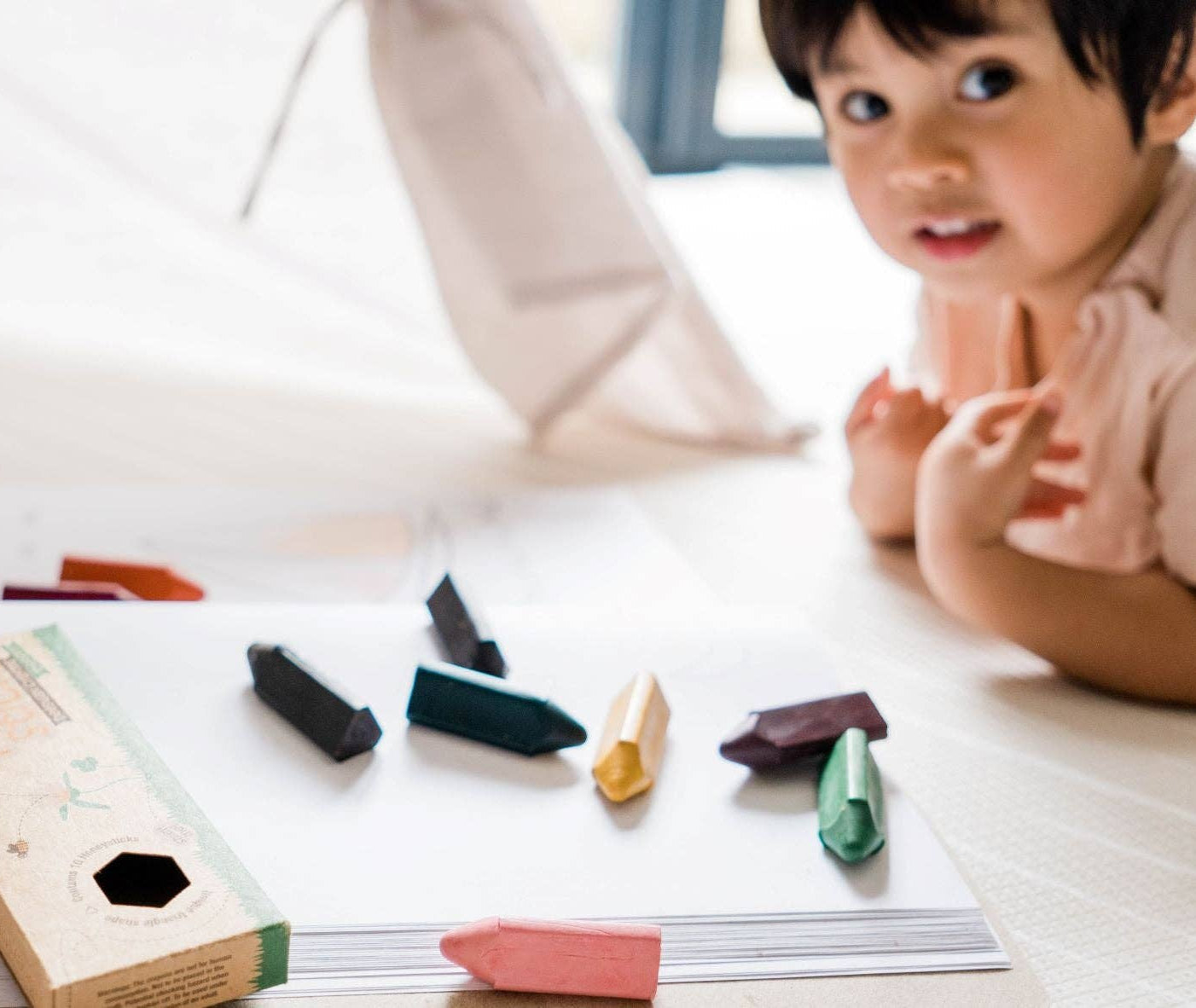 child laying on the floor drawing with triangle beeswax crayons