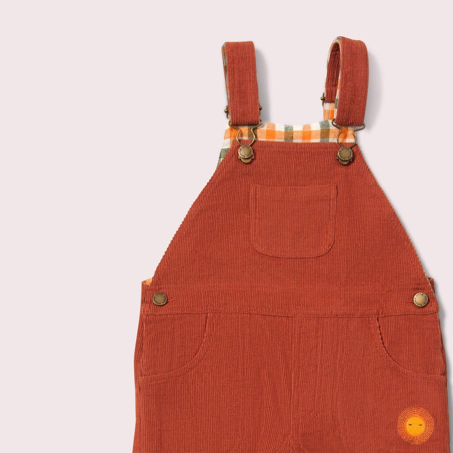 Orange corduroy overalls with plaid lining on a light gray background
