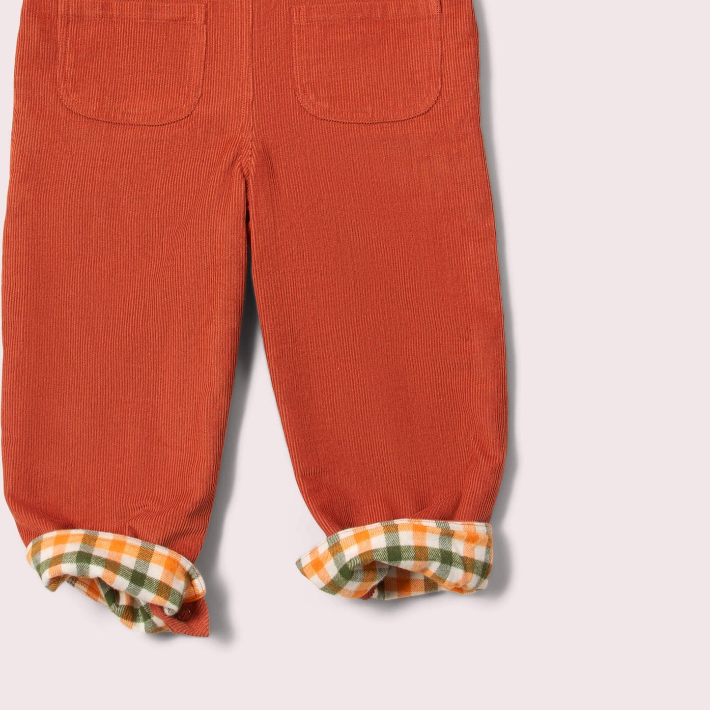 Orange corduroy overalls with plaid cuffs lining on a light gray background