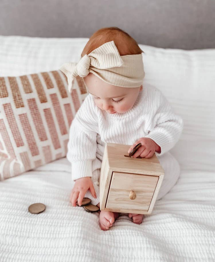 Baby playing with a wooden toy discs post box on a bed