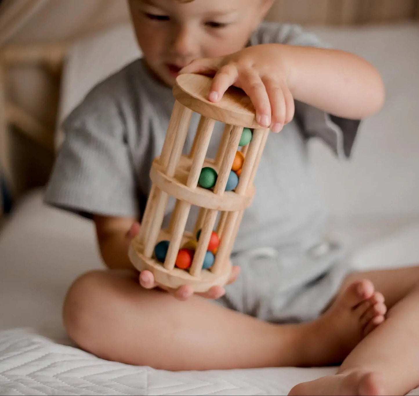 a child sitting on a bed playing with wooden mini rain maker