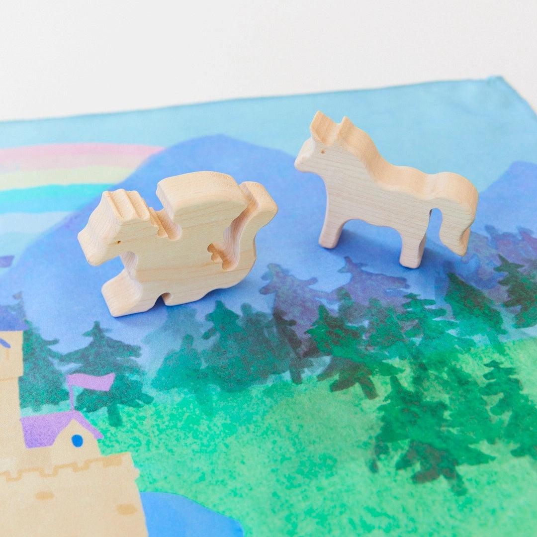 wooden unicorn and dragon figurines standing on a playsilk