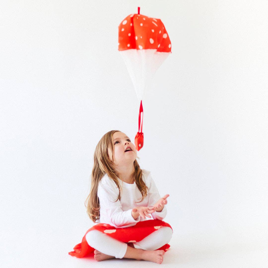 Child playing with a silk mushroom parachute against a white background