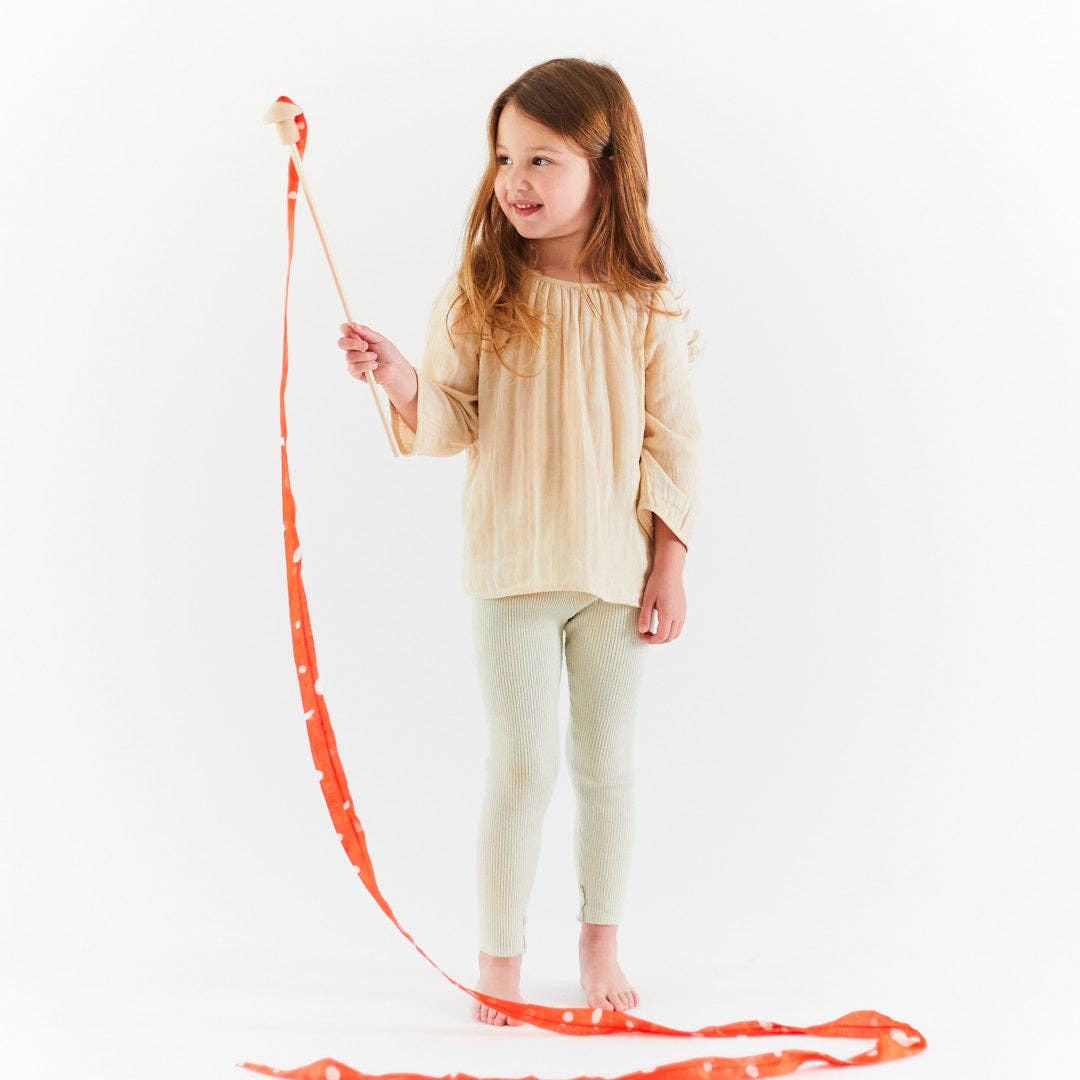 Young child holding a long red ribbon on a mushroom wand on a white background