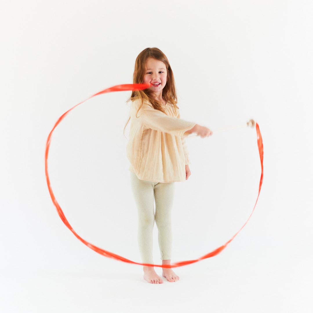 Young child playing with a red mushroom streamer wand on a white background