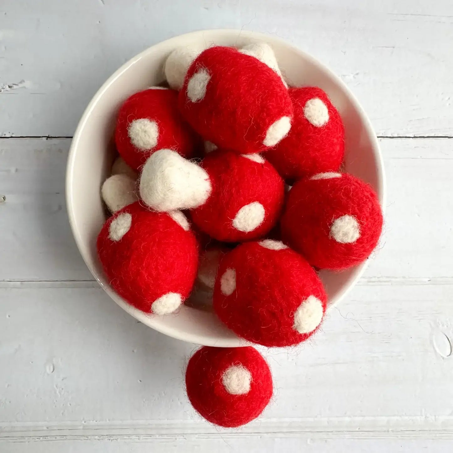 a ceramic bowl filled with felt red mushrooms