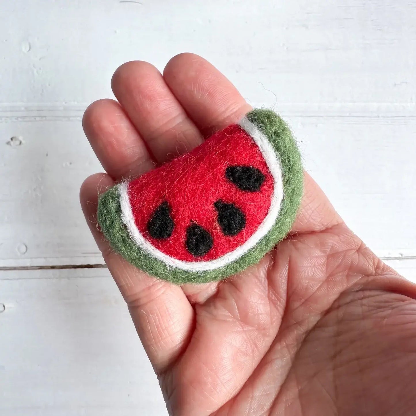 a hand holding a felt watermelon slice