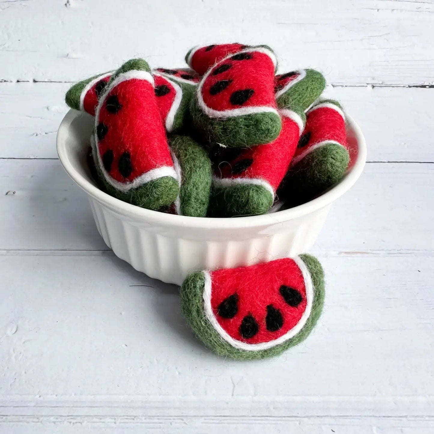 a ceramic bowl full of felt watermelon slices on a wooden table