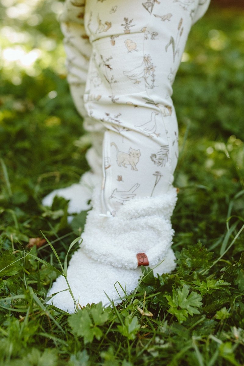 White patterned leggings with white fuzzy booties on a grassy background