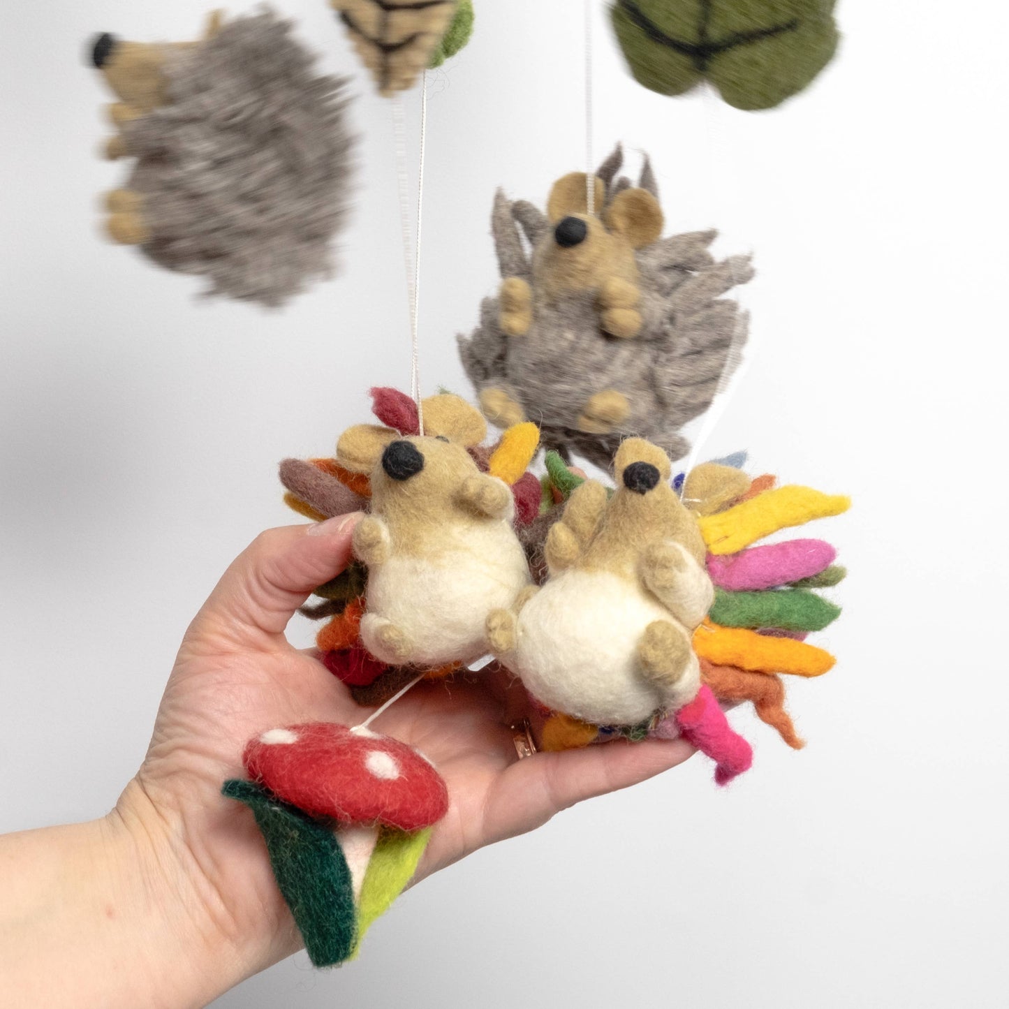 Hand holding a small rainbow hedgehog mobile parts with colorful leaves on a white background
