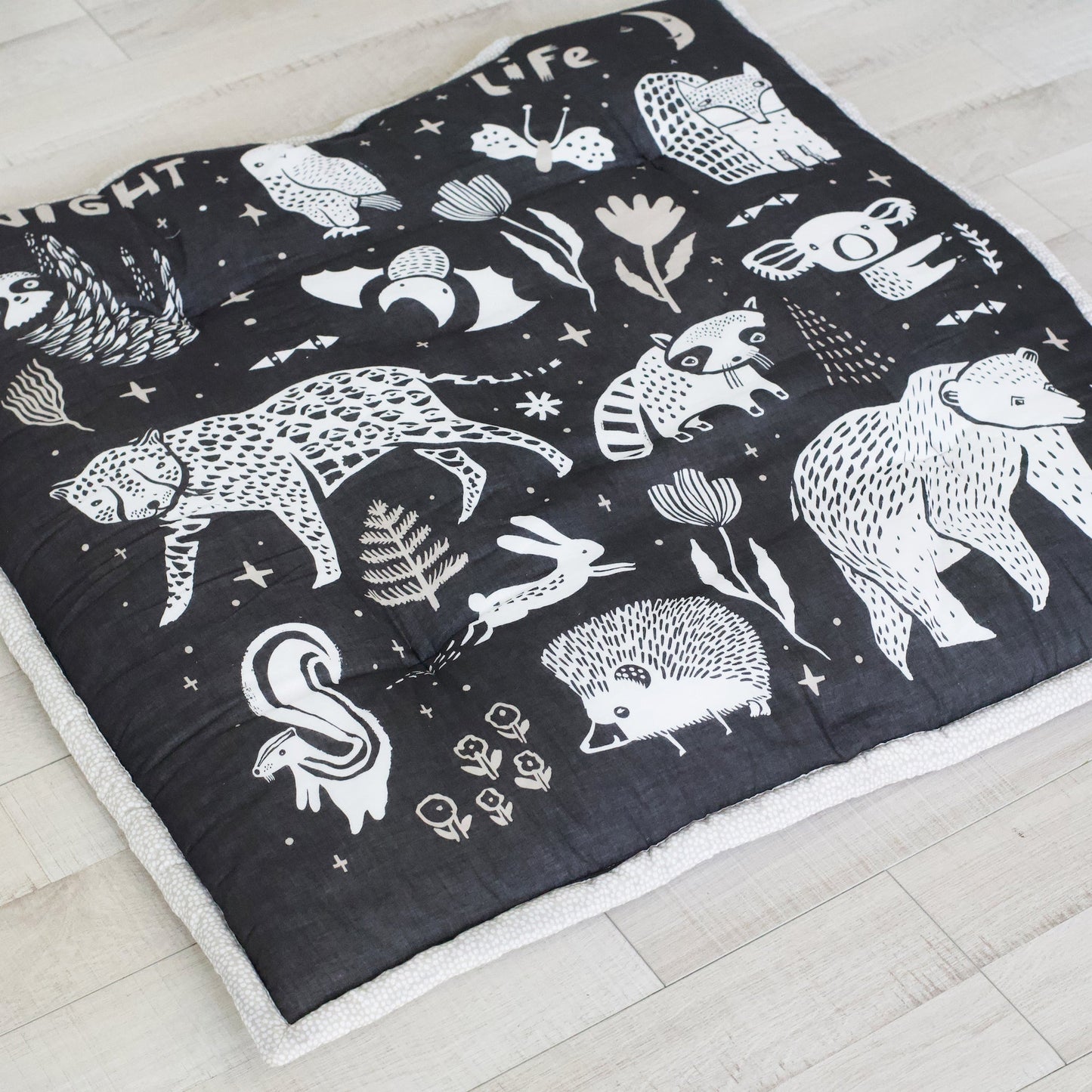 Black quilt with white animal illustrations on a light wooden floor