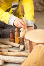 Load image into Gallery viewer, A child sitting on the floor, playing with three wooden peg people, wooden sticks and trunks
