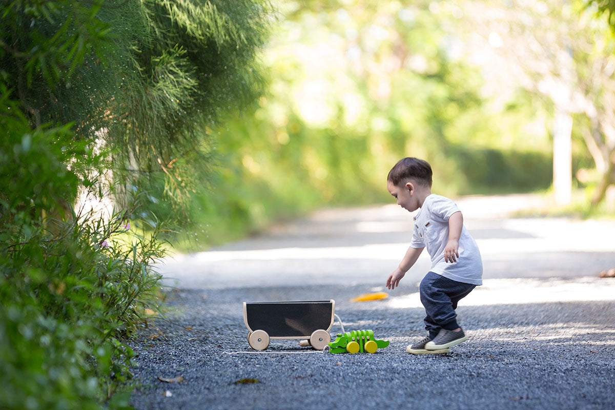 Child playing out side with Plan toys Black Wagon and alligator pull toy