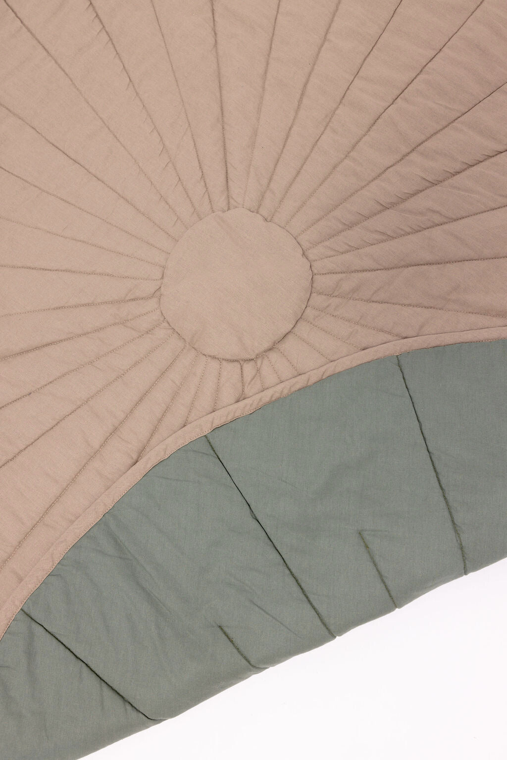 Close-up of a quilt with sunburst pattern in beige and solid color at the bottom on a white background