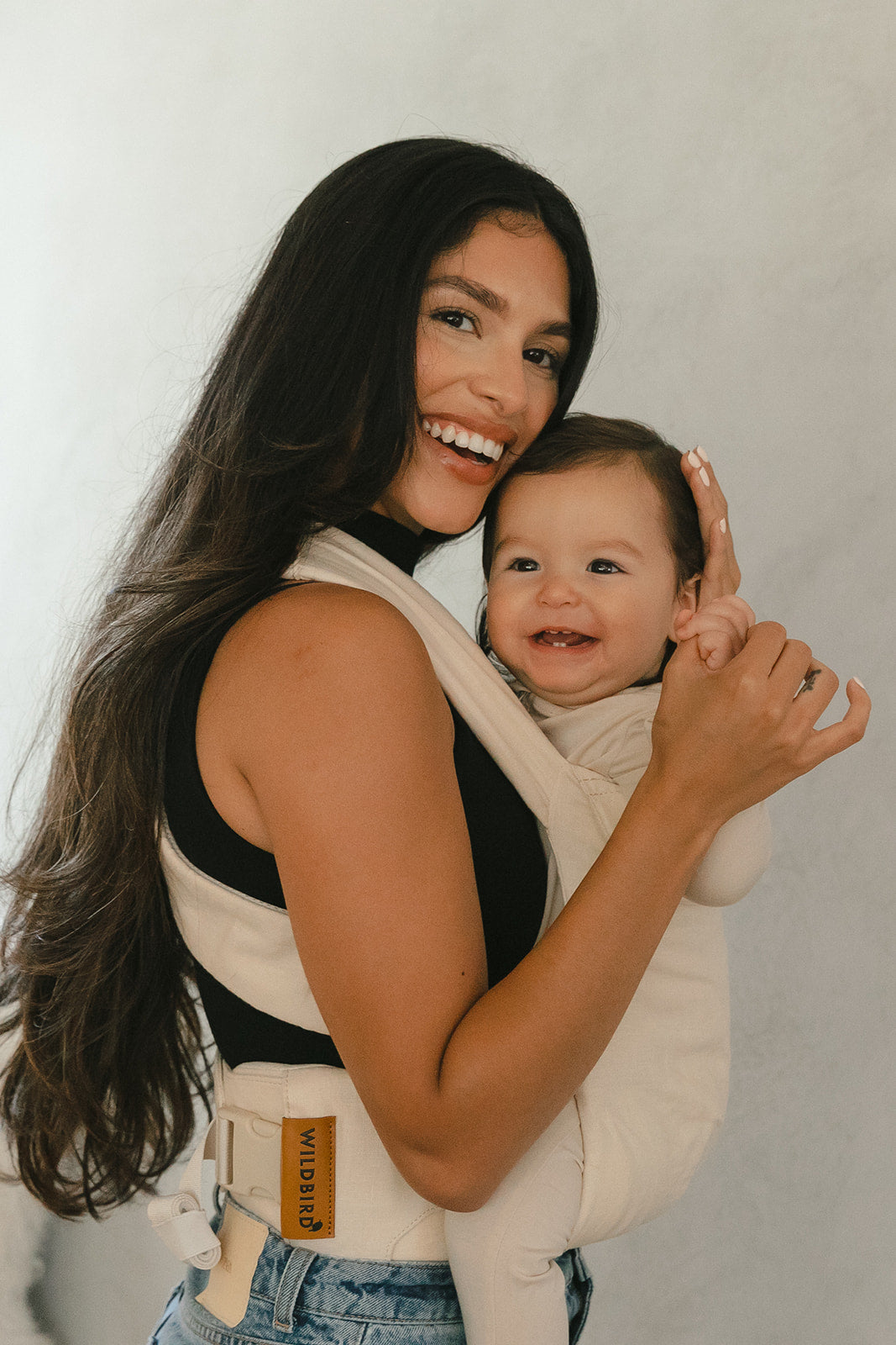 Woman holding a baby in a carrier against a plain background