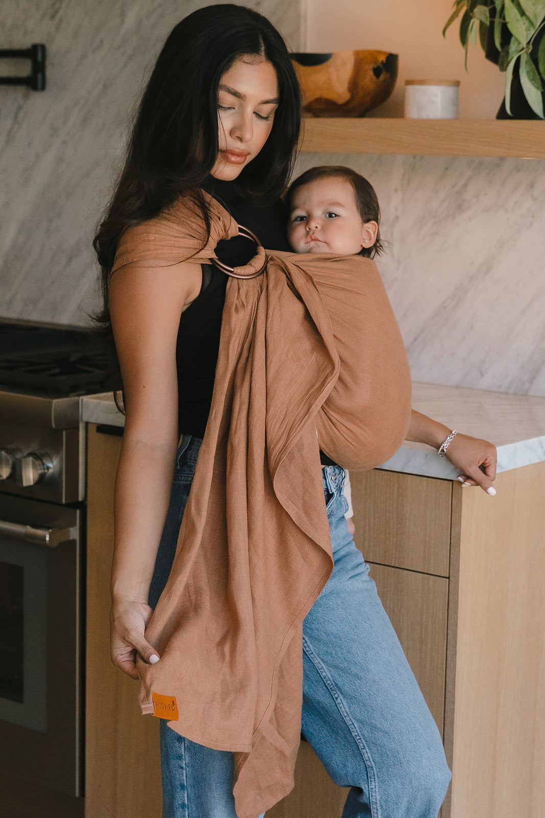 Woman holding a baby in a sling in a kitchen