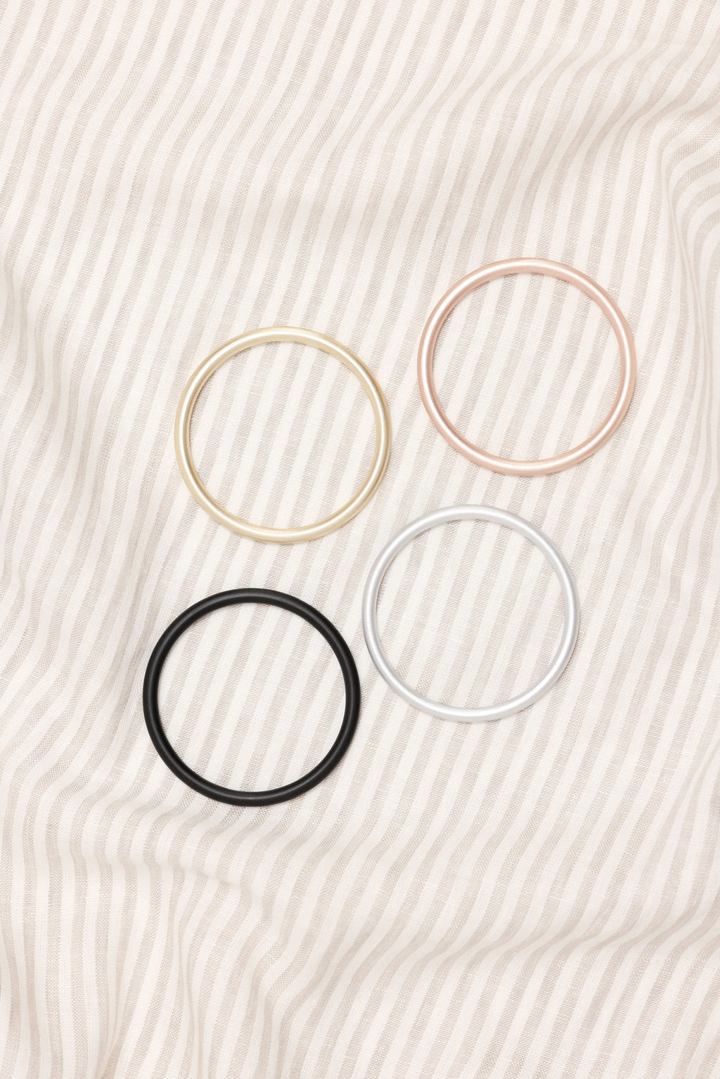 Four hair ties in gold, pink, black, and white on a textured beige background