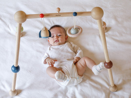 baby laying on a bed playing with Play Gym in orchard