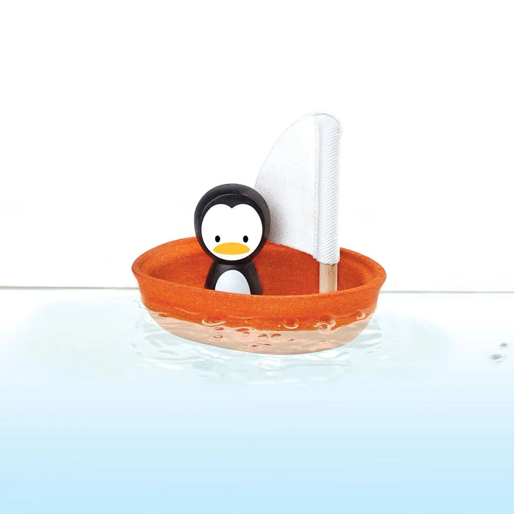 Toy penguin in an orange boat with a white sail on a light blue background
