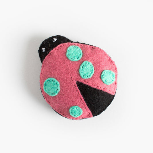 Pink ladybug-shaped toy with green spots on a white background