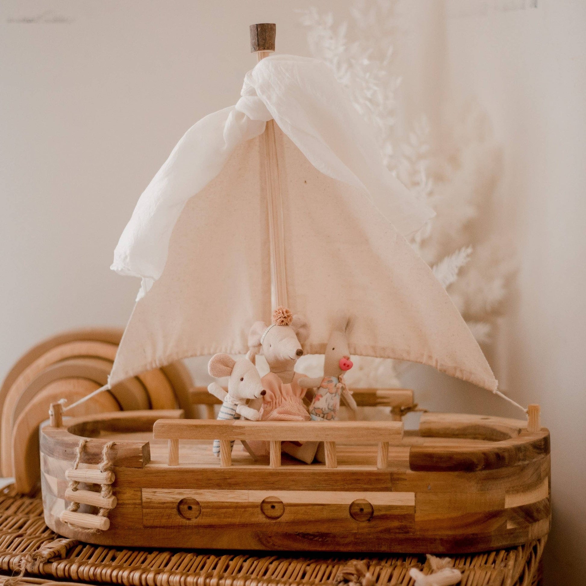 Wooden toy boat with a sail and small figurines on a textured surface.