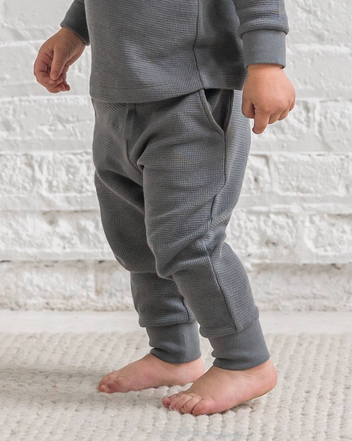 Child wearing gray waffle knit pajama set on a white textured background