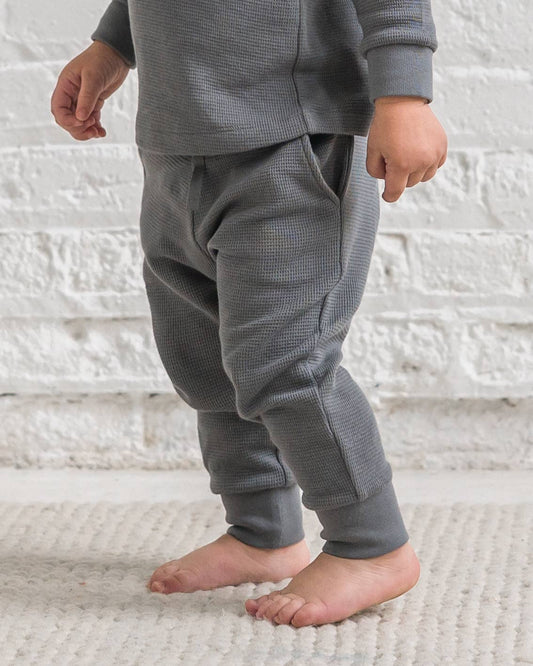 Child wearing gray waffle knit pajama set on a white textured background