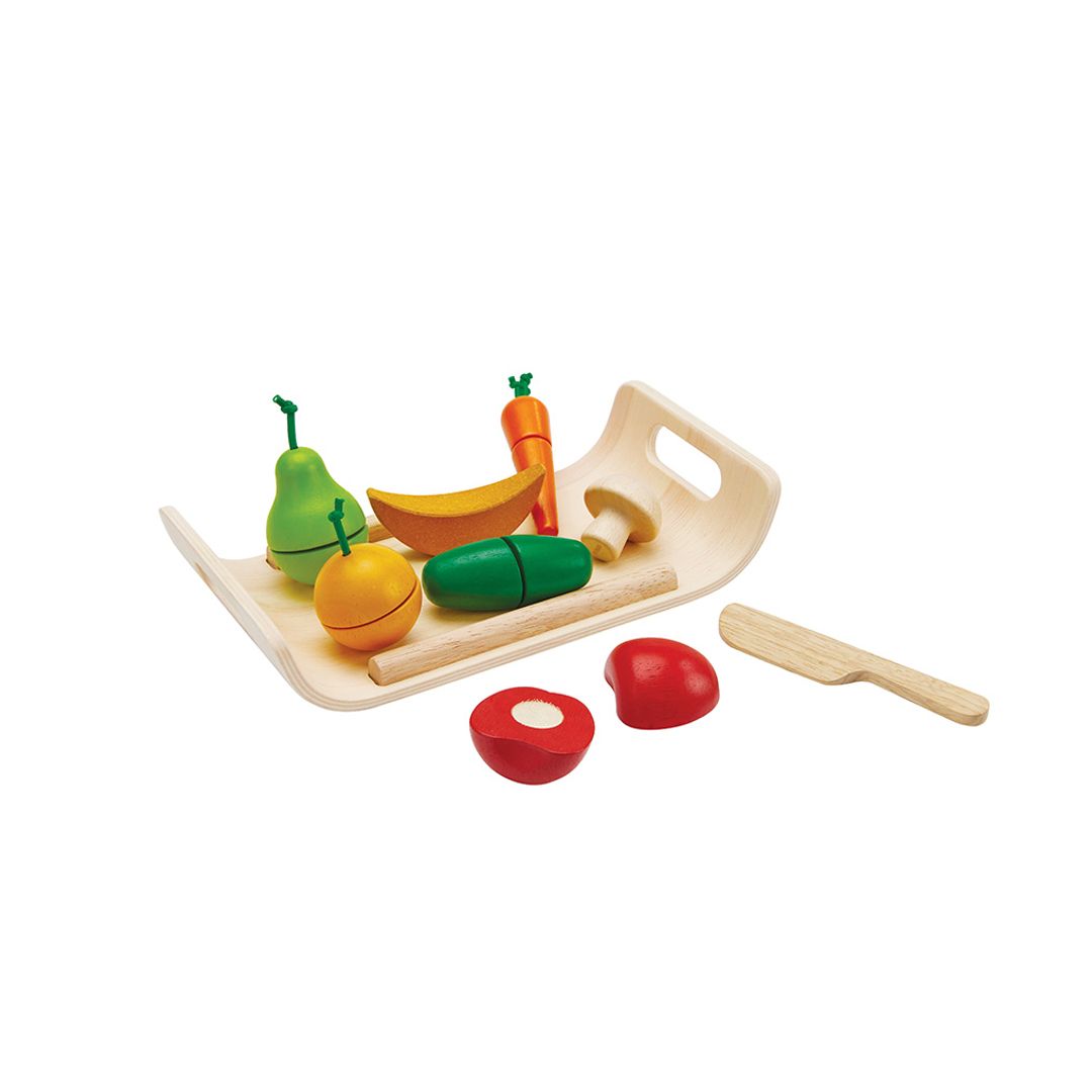 Colorful toy fruits and vegetables on a wooden tray with a knife on a white background