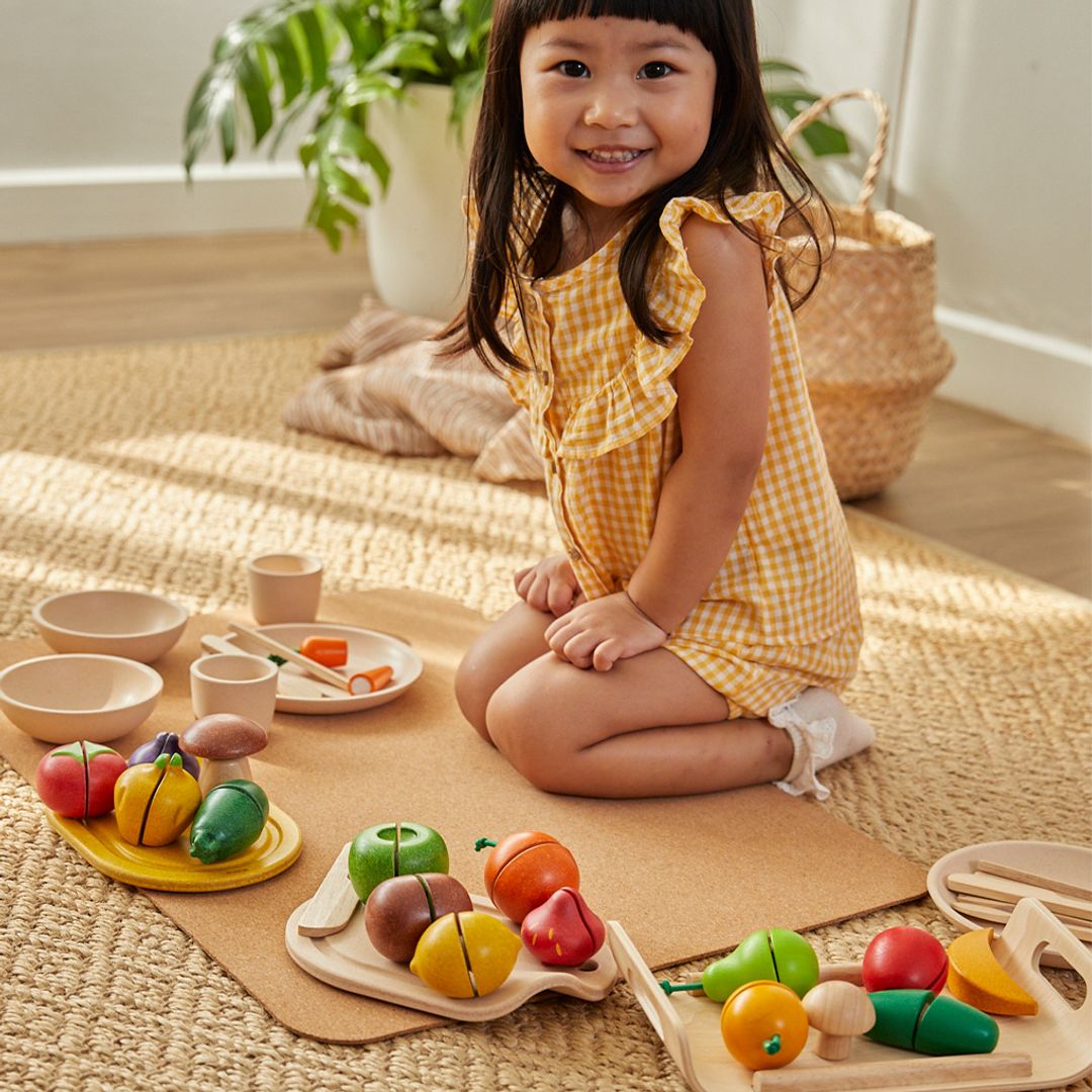 Child playing with wooden toy fruits and vegetables on a mat indoors.