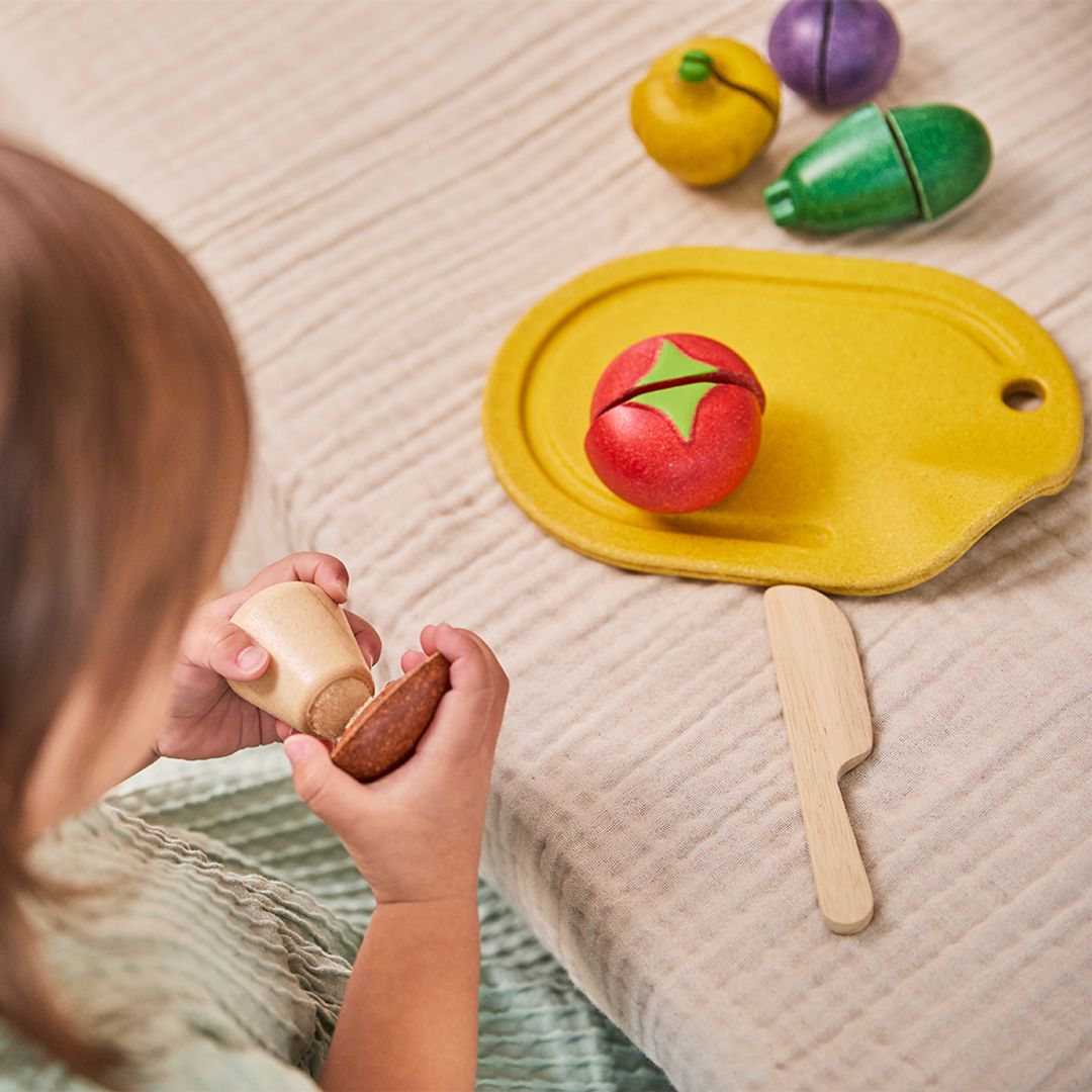 Child playing with wooden toy food items on a textured surface