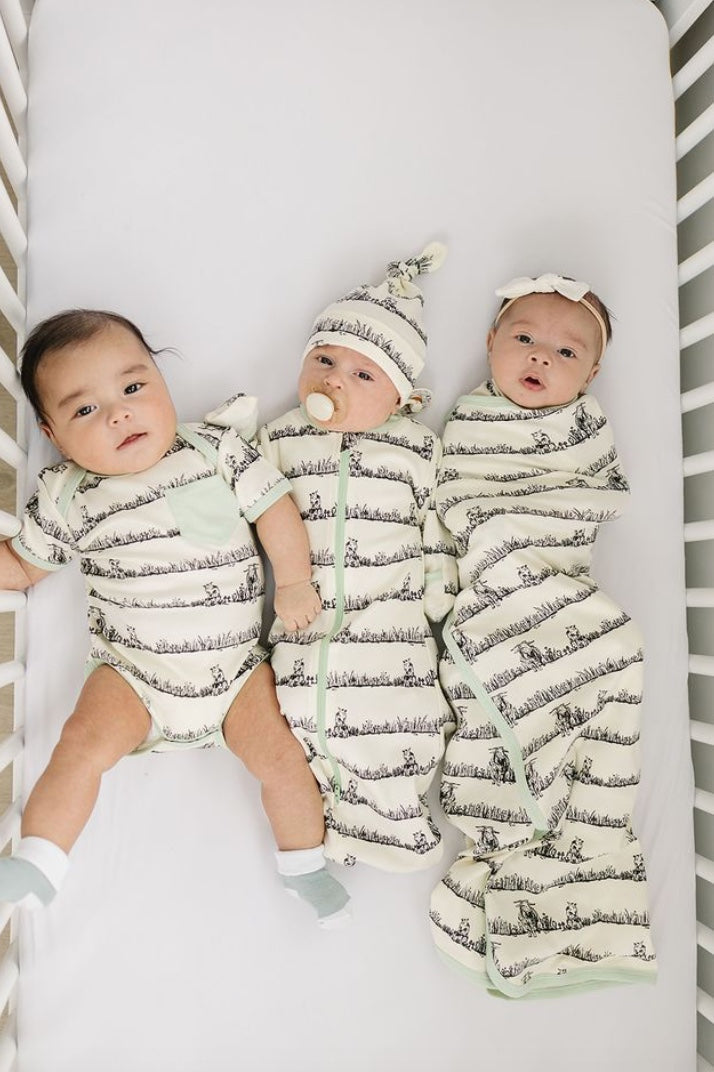 Three babies in matching outfits lying in a crib.