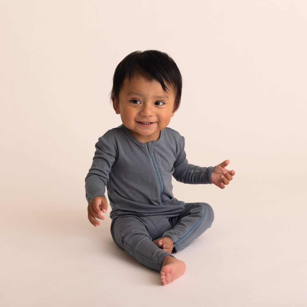 baby wearing a gray romper sitting on a beige background
