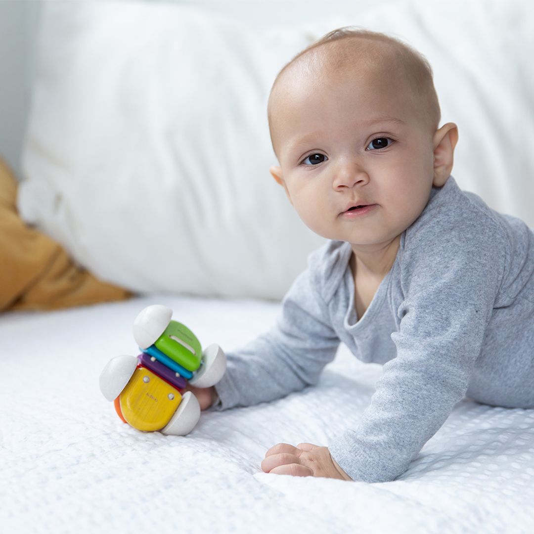 Baby lying on a bed with a colorful toy