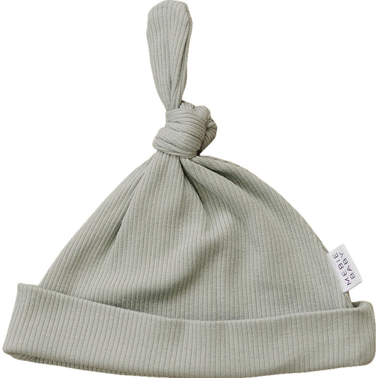 Light green ribbed baby hat with a knot on top and a label on a white background
